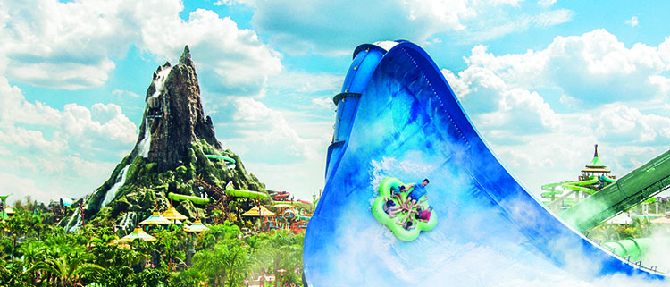 Guests in a raft slide up the side of the Honu water slide with the volcano in the background at Universal's Volcano Bay.